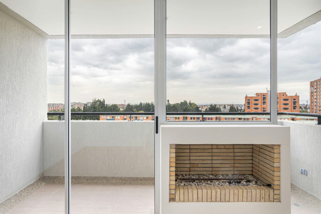 Spacious balcony with glass windows and a brick fireplace overlooking Bogot谩 cityscape.